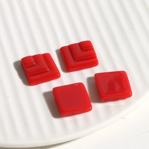 Macro view of red square resin jewelry charms with layered geometric design on ceramic tray