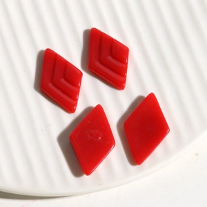Macro detail of red resin rhombus jewelry charms with V-shaped texture on white ceramic tray