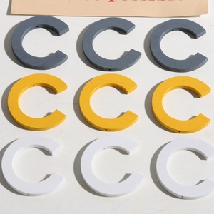 Dettaglio macro di nove ciondoli in legno a forma di C in grigio, giallo e bianco per gioielli