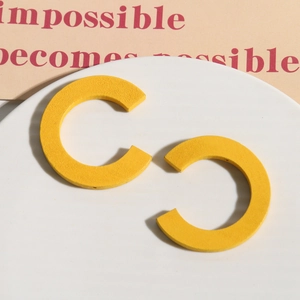 Dettaglio degli orecchini a cerchio a C in legno giallo opaco su supporto bianco