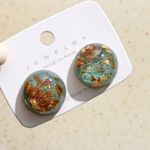Détail de boucles d'oreilles en résine bleue avec feuilles d'or et fleurs séchées