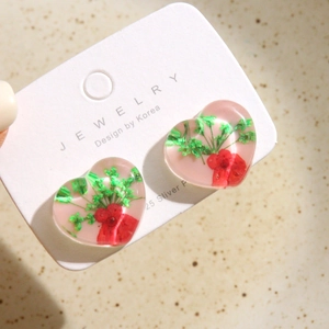 Détail de boucles d'oreilles cœur en résine avec fleurs séchées sur carte bijoux