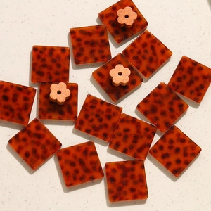 Dettaglio di ciondoli quadrati in acetato tartarugato ambra con piccoli fiori in legno delicati