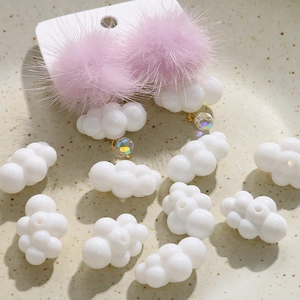 Macro shot of fluffy pink pompom cloud earrings and white DIY acrylic charms on a ceramic tray