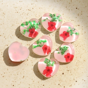 Détail macro de breloques en résine en forme de cœur avec de vraies fleurs séchées rouges