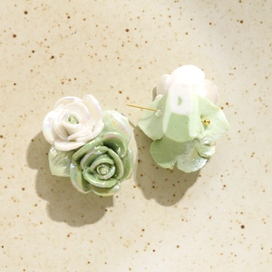 Vue détaillée des clous d'oreilles roses en céramique nacrée avec pétales blancs et verts