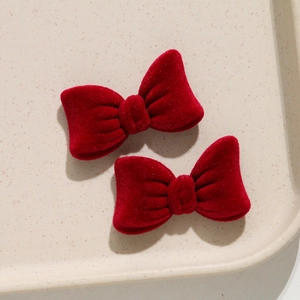 Close-up of two red velvet bow hair clips on a minimalist beige display tray