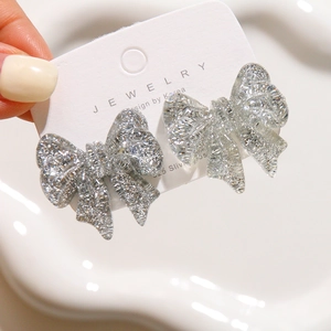 Sparkling silver bow earrings with 925 silver needles shown on a white display card