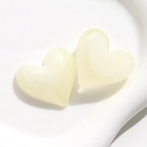 Dettaglio di due ciondoli a cuore in resina color crema su un vassoio di ceramica
