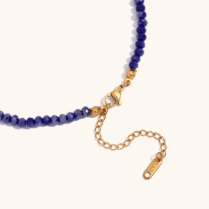 Detail van donkerblauwe gefacetteerde kralenketting met 18K vergulde sluiting en label