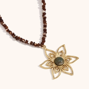 Macro detail of vintage 18K gold petal pendant with green gemstone and beaded chain