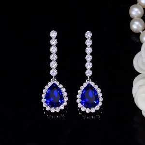 Macro shot of silver bridal earrings featuring blue pear-cut zircon with halo setting