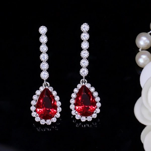 Detail of elegant silver drop earrings with pear-cut red gems and white zircon halo