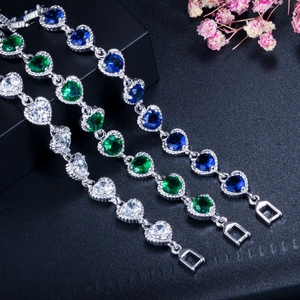 Nahaufnahme von herzförmigen Zirkon-Armbändern in Weiß, Grün und Blau auf schwarzem Display