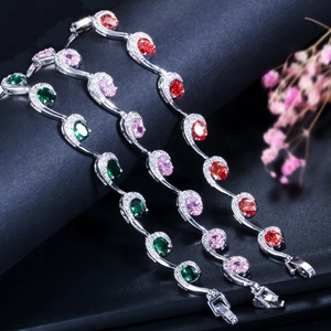 Detailopname van S-vormige zilveren armbanden met smaragd, roze en granaat stenen
