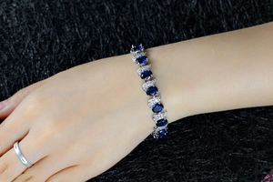 Close-up of a silver-tone bracelet featuring oval blue stones and zircons on a model's wrist
