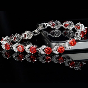 Primer plano de pulsera plateada con gemas rojas y detalles de alas de cristal blanco