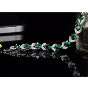 Vista macro de pulsera plateada con gemas verdes redondas y detalles de diamantes