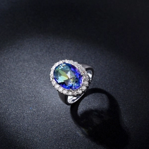 Primer plano de anillo con topacio místico ovalado y halo de circonitas en fondo negro