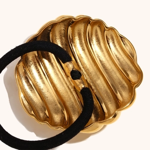 Gold textured wavy shell hair tie with black elastic band on a cream background