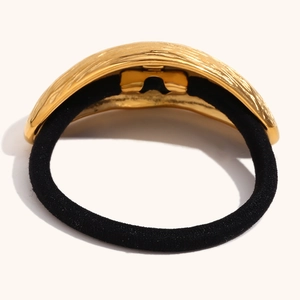 Detail of 18K gold plated metal accessory with olive shell texture on black hair tie