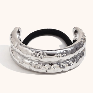 Silver hammered metal hair tie with irregular textured finish on minimalist beige background