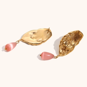 Detail of 18K gold-plated wing earrings with hammer texture and pink cat-eye stone
