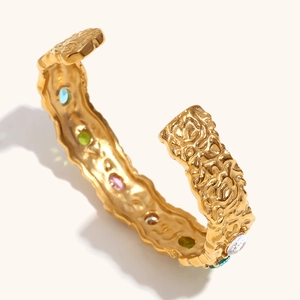 Detailed close-up of a golden wavy bangle with multi-color stones and hammered texture