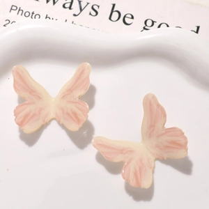 Macro view of gradient pink resin butterfly charms displayed on a ceramic jewelry tray