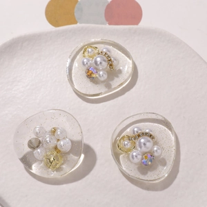 Detailed view of DIY resin bow charms with pearls, gold rings and sparkles on a tray