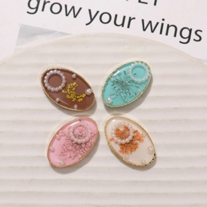 Macro view of oval resin floral charms with dried flowers and pearls in gold frames