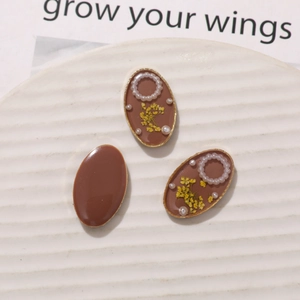 Macro detail of oval resin charms with dried flowers and pearls on white ceramic plate