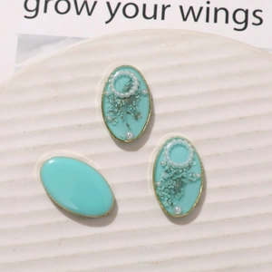 Macro detail of oval light blue resin charms with dried flowers and metallic edges