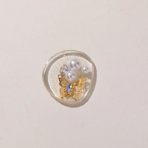 Detailed top view of a resin craft charm featuring golden butterflies and white pearls