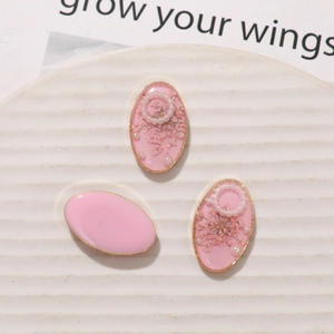 Detail of oval resin charms with pink dried flowers, pearls and gold metal base