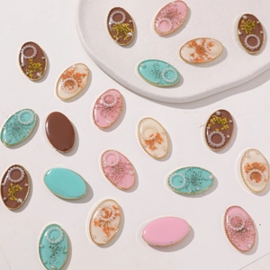 Detailed flat lay of oval resin charms with dried flowers and pearls for DIY jewelry