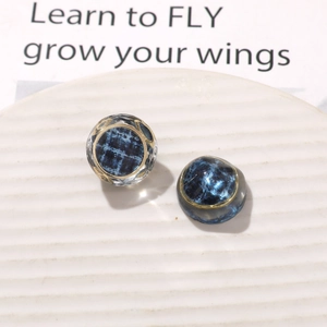 Macro detail of vintage resin earrings featuring blue tweed pattern and gold metal edges