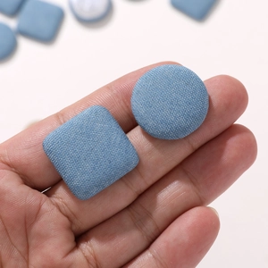 Light blue denim fabric covered round and square decorative buttons held in hand for DIY