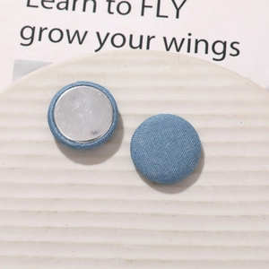 Macro detail of round light blue denim fabric buttons with flat silver metal base backs