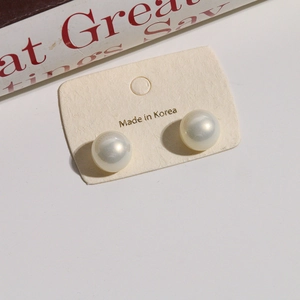 Close-up of 12mm iridescent gradient faux pearl stud earrings on a beige display card