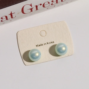 Detail of 12mm gradient mermaid pearl stud earrings on a branded white display card