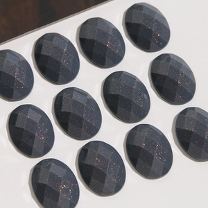 Detailed macro view of 12 oval black gold sand resin cabochons with sparkling faceted surfaces
