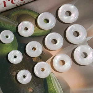 Close-up of iridescent shell-like donut beads for DIY jewelry on avocado green magazine