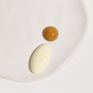 Flat lay of caramel round and beige oval resin cabochons on a white textured ceramic tray