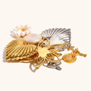 Assortimento di perle barocche, ciondoli a cuore dorati e charms a conchiglia su sfondo beige