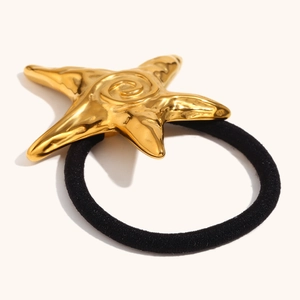 Macro detail of golden starfish hair tie with hammered texture and black elastic band