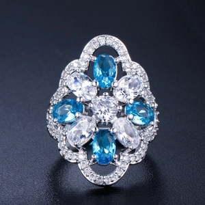 Macro detail of a flower-shaped ring with blue and white zircons on a dark surface