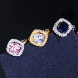 Macro shot of square-cut cubic zirconia rings in pink, blue, and white with halo setting