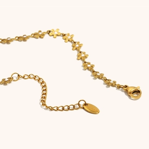 Detailaufnahme der goldenen Edelstahlkette mit weißen Emaille-Blumenanhängern