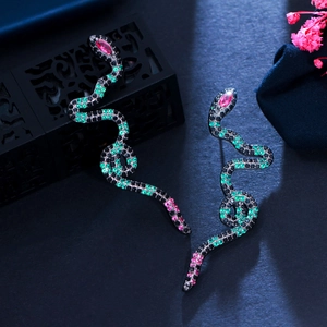 Macro detail of snake earrings with green and pink zircon stones on dark texture
